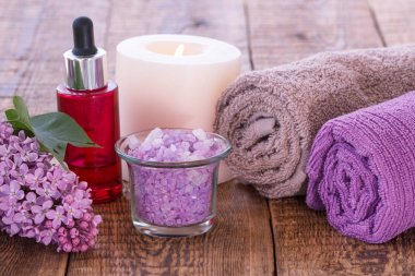 Aromatik yağ, mum, deniz tuzu ve ahşap kurullarında banyo yordamlar için havlu ile kase yazma Eflatun çiçekler, kırmızı şişe. Spa Ürünleri ve aksesuarları
