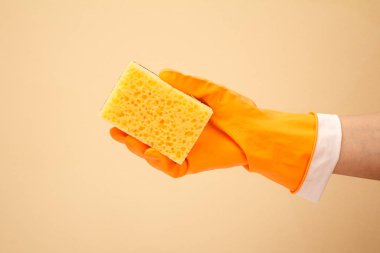 Bej arka planda sünger olan koruyucu eldivenli bir kadın eli..