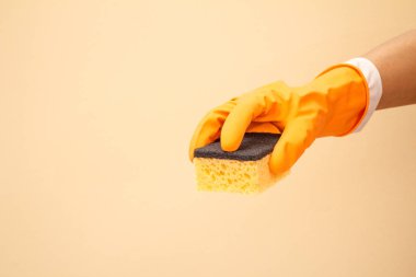 Bej arka planda sünger olan koruyucu eldivenli bir kadın eli..