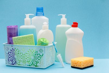 Sepette bulaşık sıvısı şişeleri, mavi arka planda sünger ler ve fırçalar.