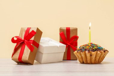 Hediye kutuları ve bej arka planda yanan şenlikli mum ile doğum günü muffin.