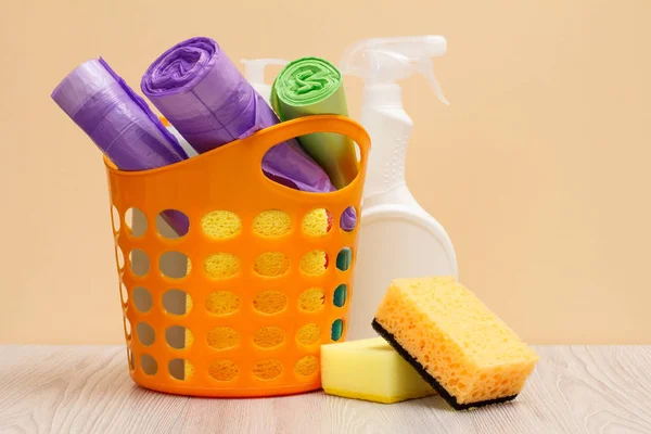 Botellas de líquido lavavajillas, cesta con bolsas de basura y esponjas en escritorio de madera . — Foto de Stock