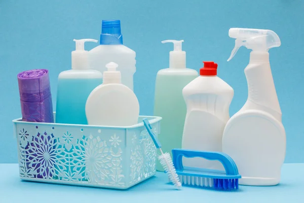 Бутылки жидкости для мытья посуды в корзине, губки и щетки на синем фоне . — стоковое фото