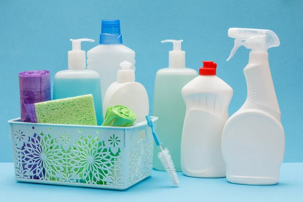 Botellas de líquido lavavajillas en cesta, esponjas y cepillos sobre fondo azul . — Foto de Stock