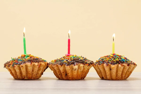 Születésnapi teasütemények égő ünnepi gyertyák bézs háttér. — Stock Fotó