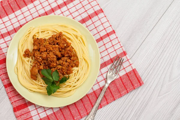 Spaghetti bolognese on a plate with metal fork and napkin.
