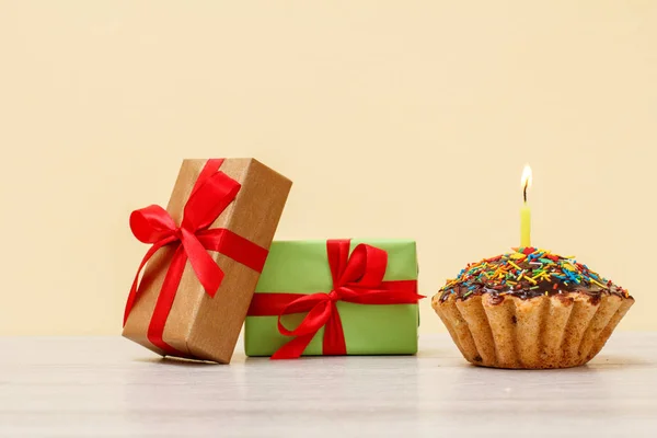 Ajándékdobozok és ízletes szülinapi muffin égő ünnepi gyertyákkal bézs alapon. — Stock Fotó