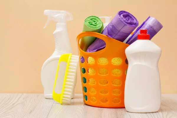 Botellas de líquido lavavajillas, cesta con bolsas de basura y cepillo en escritorio de madera . — Foto de Stock