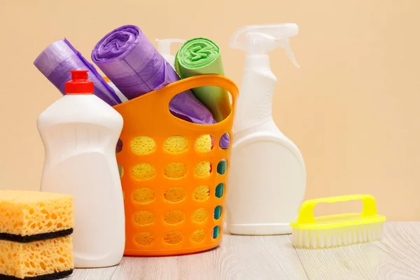 Botellas de líquido lavavajillas, cesta con bolsas de basura, cepillo y esponjas en escritorio de madera . — Foto de Stock