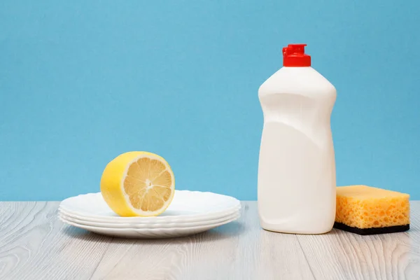 Botella de líquido lavavajillas, esponja, platos y limón sobre fondo azul . — Foto de Stock