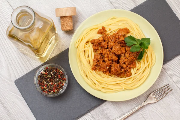 Espaguetis boloñeses en un plato con tenedor de metal y botella de vino . —  Fotos de Stock