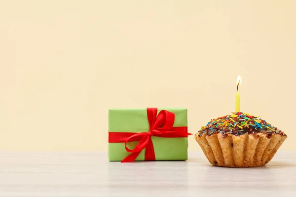 Gigt box y sabroso muffin de cumpleaños con vela festiva ardiente sobre fondo beige . — Foto de Stock