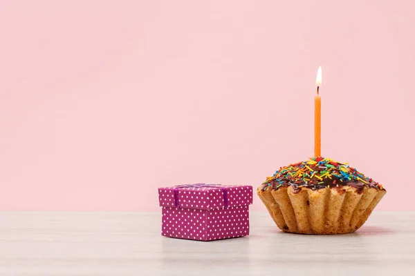 Gigt box y sabroso muffin de cumpleaños con vela festiva ardiente sobre fondo rosa . — Foto de Stock