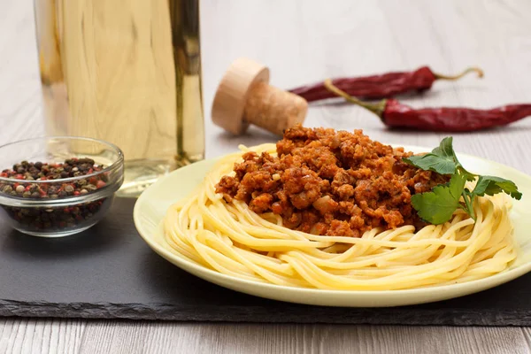 Espaguetis boloñesa en un plato, especias y una botella de vino . —  Fotos de Stock