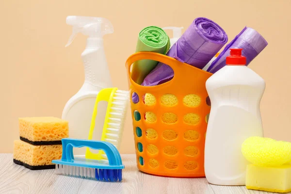 Botellas de líquido lavavajillas, cesta con bolsas de basura y esponjas en escritorio de madera . — Foto de Stock