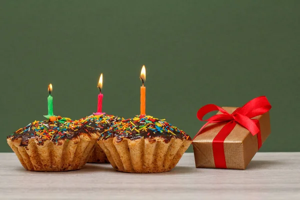 Születésnapi cupcakes égő ünnepi gyertyák és ajándék doboz zöld háttér. — Stock Fotó