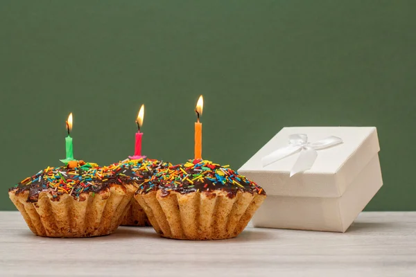 Birthday cupcakes with burning festive candles and gift box on green background. — Stock Photo, Image
