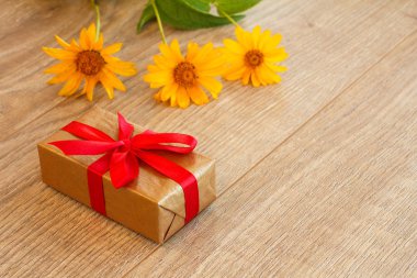 Kraft kağıdına sarılı bir hediye kutusu ve ahşap masada taze çiçekler..