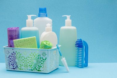 Sepette bulaşık sıvısı şişeleri, mavi arka planda sünger ler ve fırçalar.