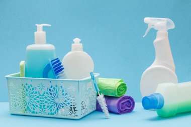 Sepette bulaşık sıvısı şişeleri, mavi arka planda sünger ler ve fırçalar.