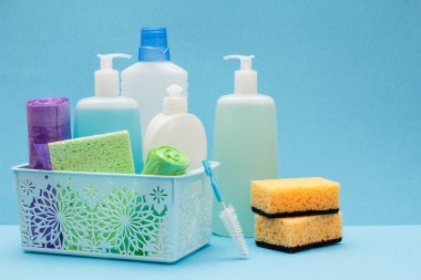 Sepette bulaşık sıvısı şişeleri, mavi arka planda sünger ler ve fırçalar.