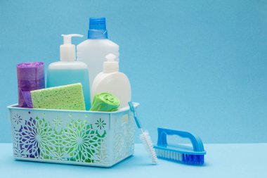 Sepette bulaşık sıvısı şişeleri, mavi arka planda sünger ler ve fırçalar.