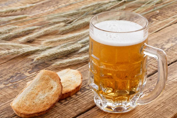Copo de cerveja com orelhas de cevada e pão em um fundo de madeira . — Fotografia de Stock