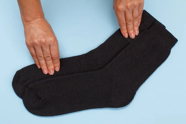 Женские руки с парой черных шерстяных мужских носков на синем фоне . — стоковое фото