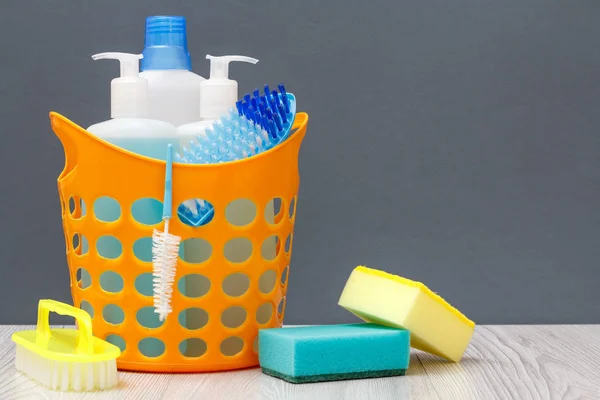 Bouteilles de liquide vaisselle dans un panier avec brosse sur bureau en bois . — Photo