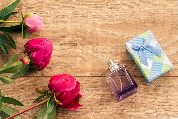 Pudełko i perfumy na drewnianych deskach z kwiatami piwonii. — Zdjęcie stockowe