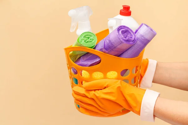 女人的手戴着防护手套和垃圾袋，还有米色背景的橙色篮子里的玻璃瓶清洁剂. — 图库照片