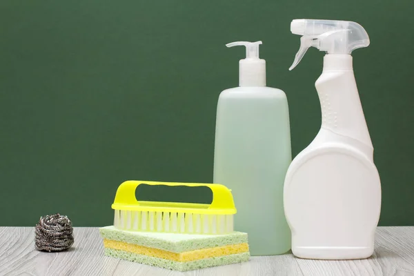 Bottles of dishwashing liquid, glass and tile cleaner, brush and sponges on green background. — Stock Photo, Image