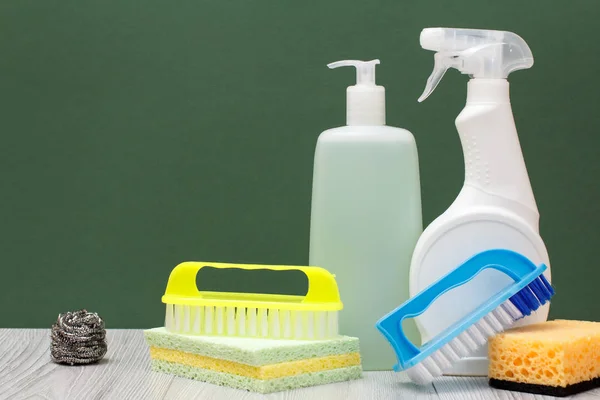 Bottles of dishwashing liquid, glass and tile cleaner, brushes and sponges on green background.