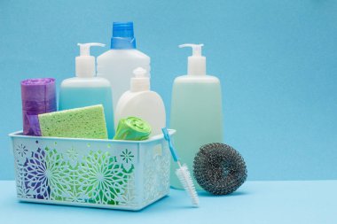 Sepette bulaşık sıvısı şişeleri, mavi arka planda sünger ler ve fırçalar.