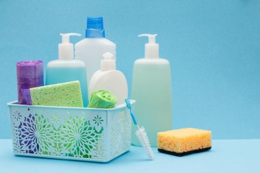 Sepette bulaşık sıvısı şişeleri, mavi arka planda sünger ler ve fırçalar.