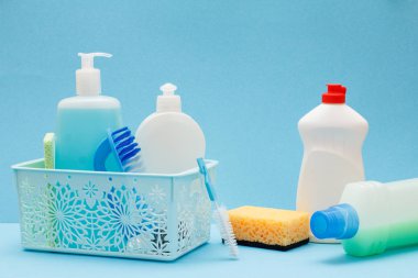 Sepette bulaşık sıvısı şişeleri, mavi arka planda sünger ler ve fırçalar.