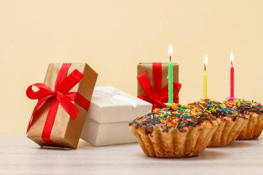 Bej arka planda yanan şenlik mumları olan hediye kutuları ve doğum günü çörekleri..