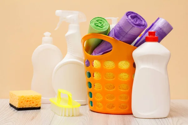 Bottles of dishwashing liquid, basket with garbage bags and sponges on wooden desk. — Stock Photo, Image