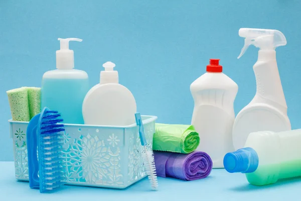 Botellas de líquido lavavajillas en cesta, esponjas y cepillos sobre fondo azul . — Foto de Stock