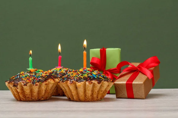 Cupcakes de cumpleaños con velas festivas ardientes y cajas de regalo sobre fondo verde . — Foto de Stock