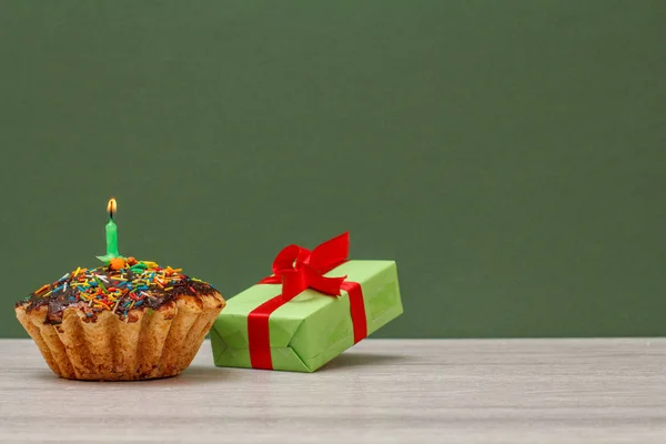 Magdalena de cumpleaños con vela festiva ardiente y caja de regalo sobre fondo verde . — Foto de Stock