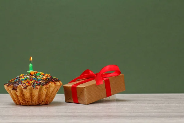 Születésnapi cupcake égő ünnepi gyertya és ajándék doboz zöld háttér. — Stock Fotó