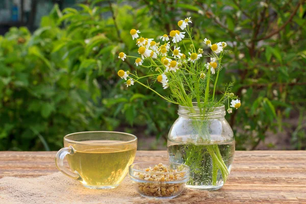 Glass cup of green tea with white chamomile flowers in a glass jar outdoor. — Stock Photo, Image