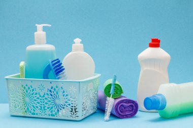 Sepette bulaşık sıvısı şişeleri, mavi arka planda sünger ler ve fırçalar.