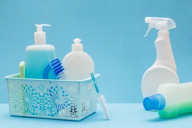 Sepette bulaşık sıvısı şişeleri, mavi arka planda sünger ler ve fırçalar.