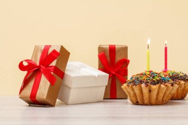 Bej arka planda yanan şenlik mumları olan hediye kutuları ve doğum günü çörekleri..