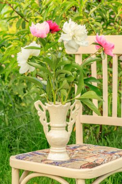 Bahçede beyaz bir sandalyede çiçek vazo.