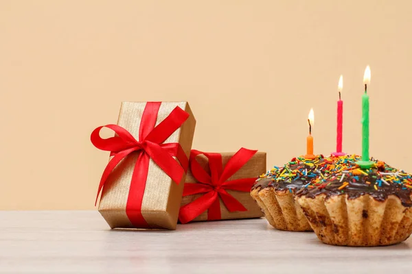 Sabroso panecillo de cumpleaños con vela festiva ardiente y cajas de regalo . — Foto de Stock