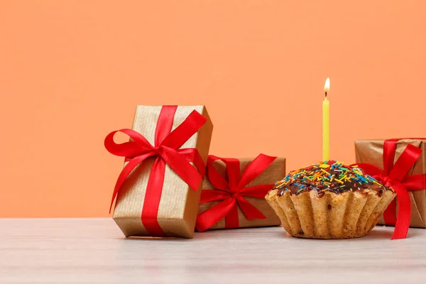 Sabroso panecillo de cumpleaños con vela festiva ardiente y cajas de regalo . — Foto de Stock