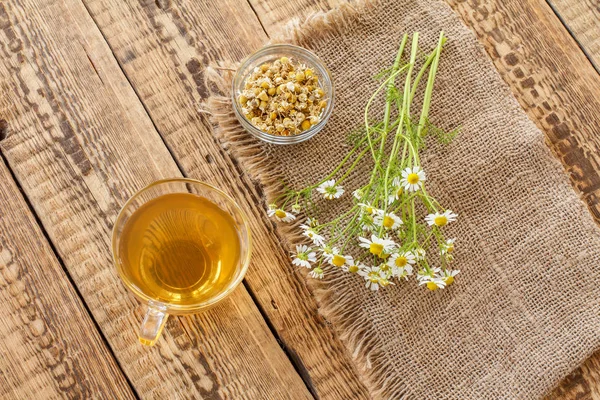 Coupe en verre de thé vert avec des fleurs de camomille blanche dans un bocal en verre . — Photo